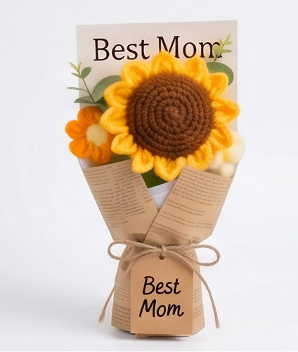 A floral arrangement is displayed in a brown paper wrap, featuring a large sunflower and decorative elements, including white pom-poms and green leaves. A tag labeled 'Best Mom' is attached at the base of the bouquet.