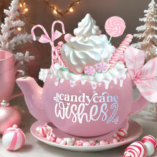 alt= A pink teapot decorated with candy canes and whipped cream, surrounded by Christmas ornaments and peppermint candies. The words "candy cane wishes" are written on the teapot.