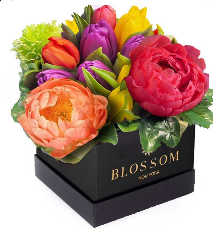 A black box labeled "Blossom New York" containing a colorful arrangement of flowers, including pink peonies, purple tulips, and orange roses, with green leaves.