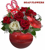 
A festive floral arrangement in a red ornament-shaped vase, featuring red and white roses, green foliage, and silver accents. Two candy canes are tucked among the flowers, enhancing the holiday theme.